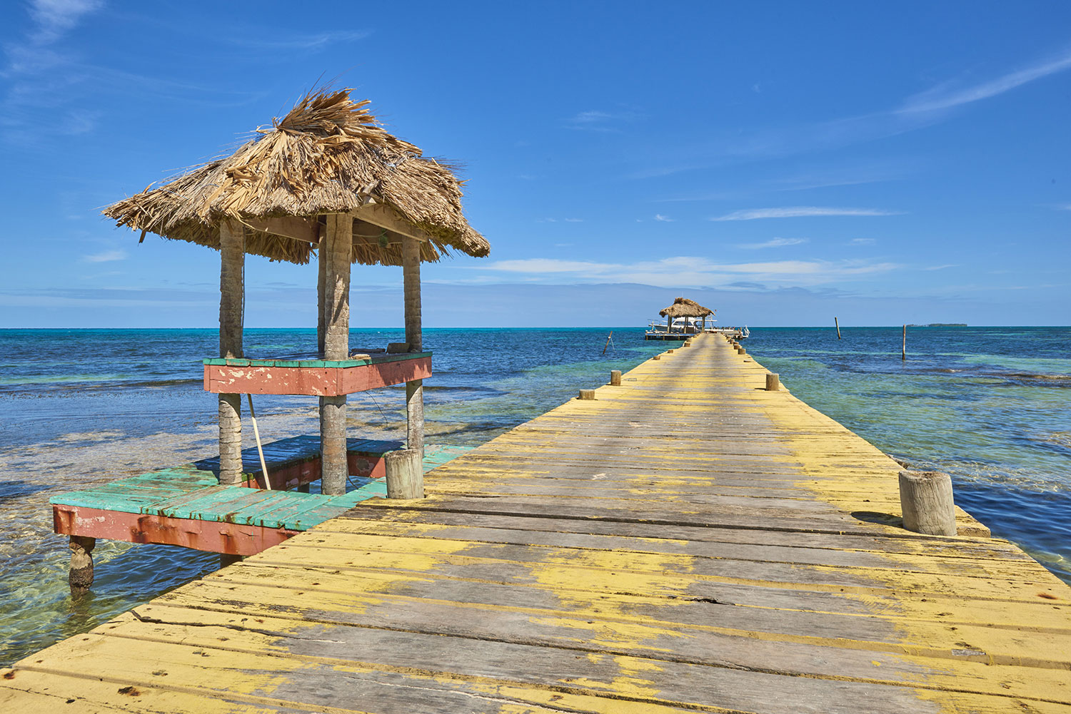 Wooden pier with yellow paint leading into the sea in Belize