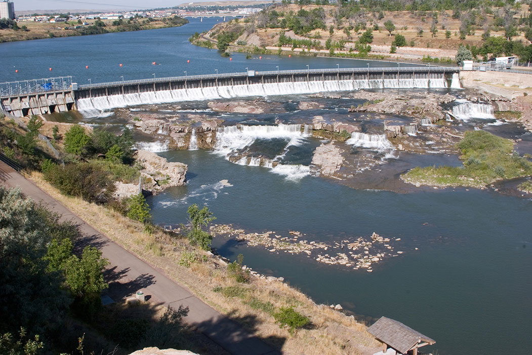 Water foams and flows over rocks by a large dam in Great Falls